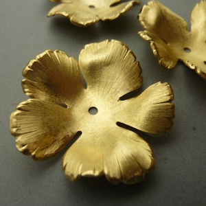 May include: Close-up of several gold-colored, five-petal flower-shaped components. Each component has a central hole and textured details on the petals. The components are likely for jewelry making or other craft projects.