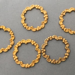 May include: Five gold-colored metal rings with a decorative, ornate design. The rings are all the same size and shape.
