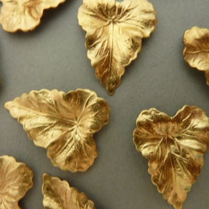 Puede incluir: Una colección de ocho hojas de metal de color dorado con un patrón de nervaduras detallado. Las hojas tienen forma de corazón y una superficie ligeramente texturizada.