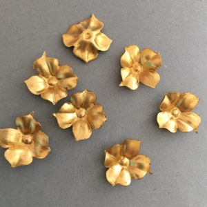May include: Six gold-colored metal flower embellishments with five petals each. The flowers have a slightly raised center.