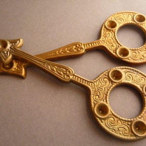 May include: A pair of antique gold-toned scissors with ornate floral designs and multiple circular cutouts. The scissors have a unique, pointed design on one end.
