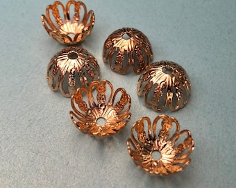 May include: Six gold-colored metal bead caps with a decorative floral design. The caps are open at the top and have a small hole in the center.