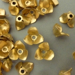 May include: A group of gold-colored metal flower-shaped embellishments. The embellishments have three petals and a hole in the center.