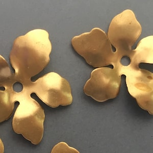 May include: Two gold metal flower-shaped charms with a hole in the centre. The charms are approximately 2.5 cm in diameter.