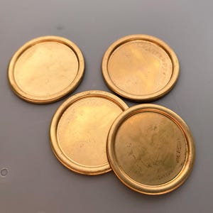 May include: Four round, gold-colored metal discs with a raised edge. The discs are smooth and shiny.