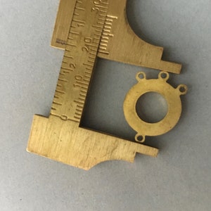May include: A brass connector with three holes, measured with a caliper. The connector is round with a hole in the center.