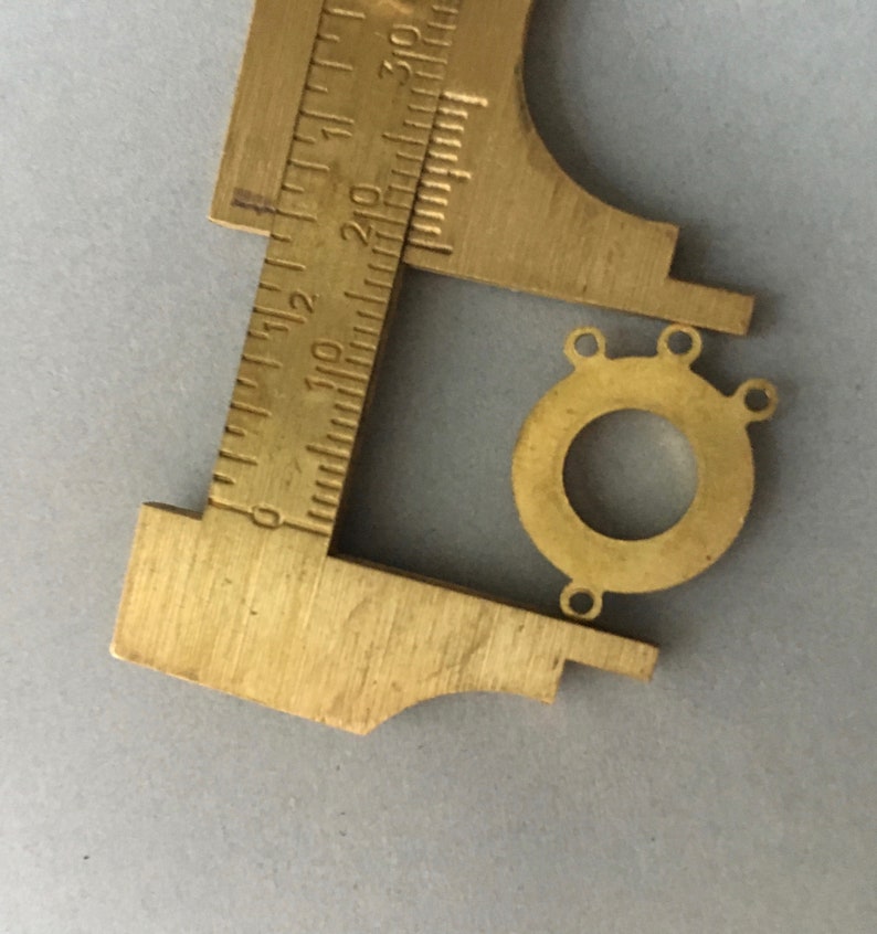 May include: A brass connector with three holes, measured with a caliper. The connector is round with a hole in the center.