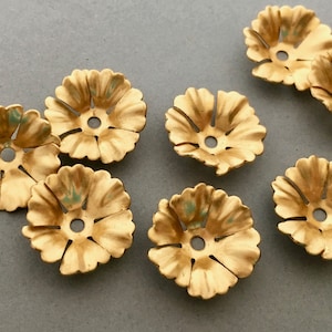 Può includere: Sette decorazioni metalliche dorate a forma di fiore con un foro al centro. Le decorazioni hanno una superficie leggermente testurizzata.