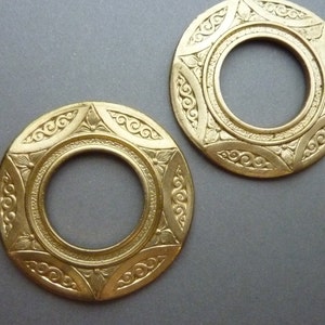 May include: Two gold-colored metal rings with intricate, ornate designs. The rings have a circular opening in the center.