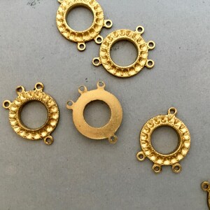 May include: Five gold-toned metal connector rings with decorative edges and three loops each. The rings are arranged on a gray surface.