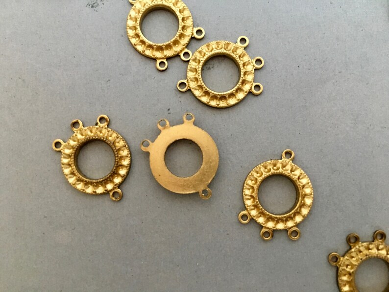 May include: Five gold-toned metal connector rings with decorative edges and three loops each. The rings are arranged on a gray surface.