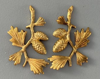 May include: Two gold-toned metal pine cone and branch ornaments. Each ornament features a pine branch with three pine needles and two pine cones.