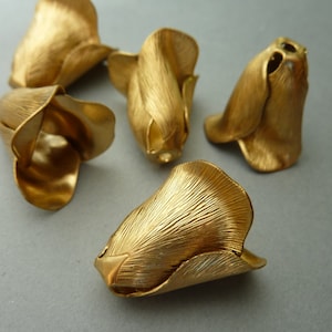 May include: Five gold-colored metal flower-shaped embellishments. The embellishments are all the same shape, but they are slightly different sizes. They have a textured surface and a slightly curved shape.