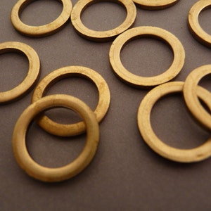 Op de afbeelding: Een groep van 10 gouden metalen ringen in verschillende maten. De ringen zijn willekeurig gerangschikt op een grijs oppervlak.
