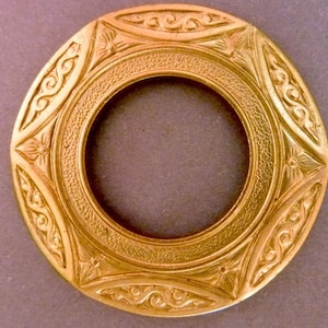 Könnte beinhalten: Ein goldfarbener Metallring mit aufwendigen gravierten Designs. Der Ring hat eine kreisförmige Öffnung in der Mitte.