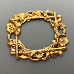 May include: Gold-toned metal frame with a floral design. The frame is square with rounded corners and features a delicate floral pattern with leaves and flowers.