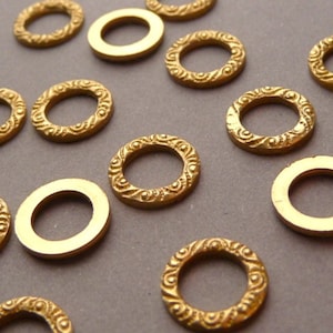 May include: A collection of gold-coloured metal rings with decorative edges. Some of the rings have a smooth finish, while others have a textured design.