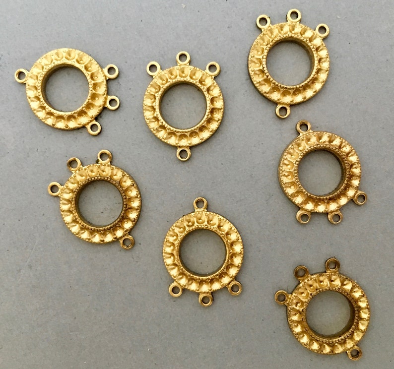 May include: Six gold-toned metal connector charms with a decorative design. Each charm has a circular center with three loops extending from the edge.
