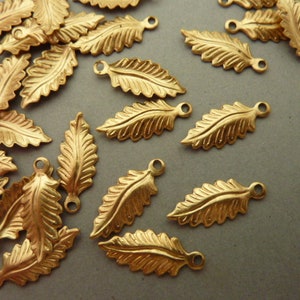 Könnte beinhalten: Eine Sammlung von goldfarbenen Metall-Blätter-Anhängern mit einem detaillierten Design. Die Anhänger haben oben ein Loch zum Anbringen an Schmuck oder anderen Bastelarbeiten.