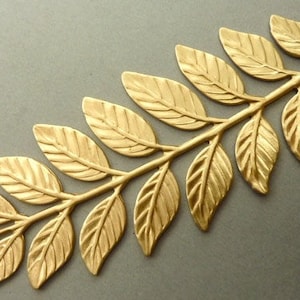 以下が含まれることがあります： テクスチャ加工された表面を持つ金色の金属の葉のガーランド。ガーランドは、細い茎でつながった個々の葉で構成されています。