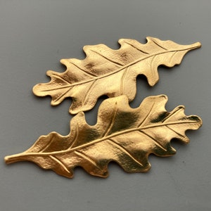 May include: Two gold-colored metal oak leaf charms. The leaves are detailed with veins and have a textured surface.