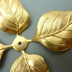 Pode incluir: Adornos de folhas de metal dourado com superfície texturizada. As folhas estão dispostas em forma de estrela de quatro pontas.