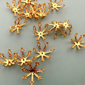 Peut inclure: Plusieurs petits capuchons de perles en métal doré, chacun avec un motif en forme d'éclat d'étoile. Les capuchons ont un trou central et de multiples bras avec des découpes en forme de losange. Ces composants décoratifs sont parfaits pour la fabrication de bijoux.