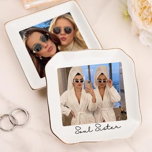 May include: Two square white ceramic trinket dishes with gold-painted edges. The front dish features a printed photograph of two people in white robes and towels with the text Soul Sister in black script. The back dish shows a photo of two people.