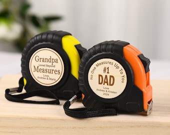 Puede incluir: Dos cintas métricas negras y amarillas con mensajes grabados en madera. Uno dice "Grandpa Loved Beyond Measures" y el otro dice "No One Measures Up To You #1 Dad".