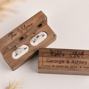 Puede incluir: Caja de anillos de madera con dos compartimentos para anillos. La caja est&aacute; grabada con "The Wilsons" en la parte superior y "George & Ashley - June 26, 2024" en la parte inferior.