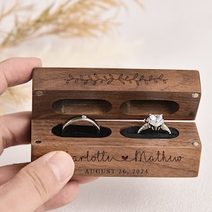 Puede incluir: Una caja de madera para anillos con dos compartimentos para anillos. La caja est&aacute; grabada con los nombres "Charlotte" y "Matthew" y la fecha "August 26, 2024".