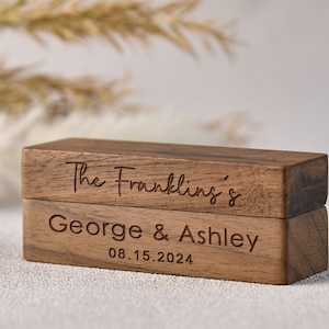 Puede incluir: Una caja de anillos de madera de dos niveles. La capa superior est&aacute; grabada con "The Franklins'" y la capa inferior est&aacute; grabada con "George & Ashley 08.15.2024".