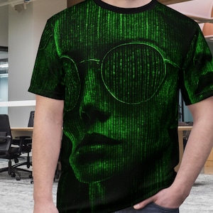 May include: Black crew neck t-shirt featuring a green digital matrix design. The graphic depicts a face wearing round glasses. The design is a digital rendering of a face with a black collar.