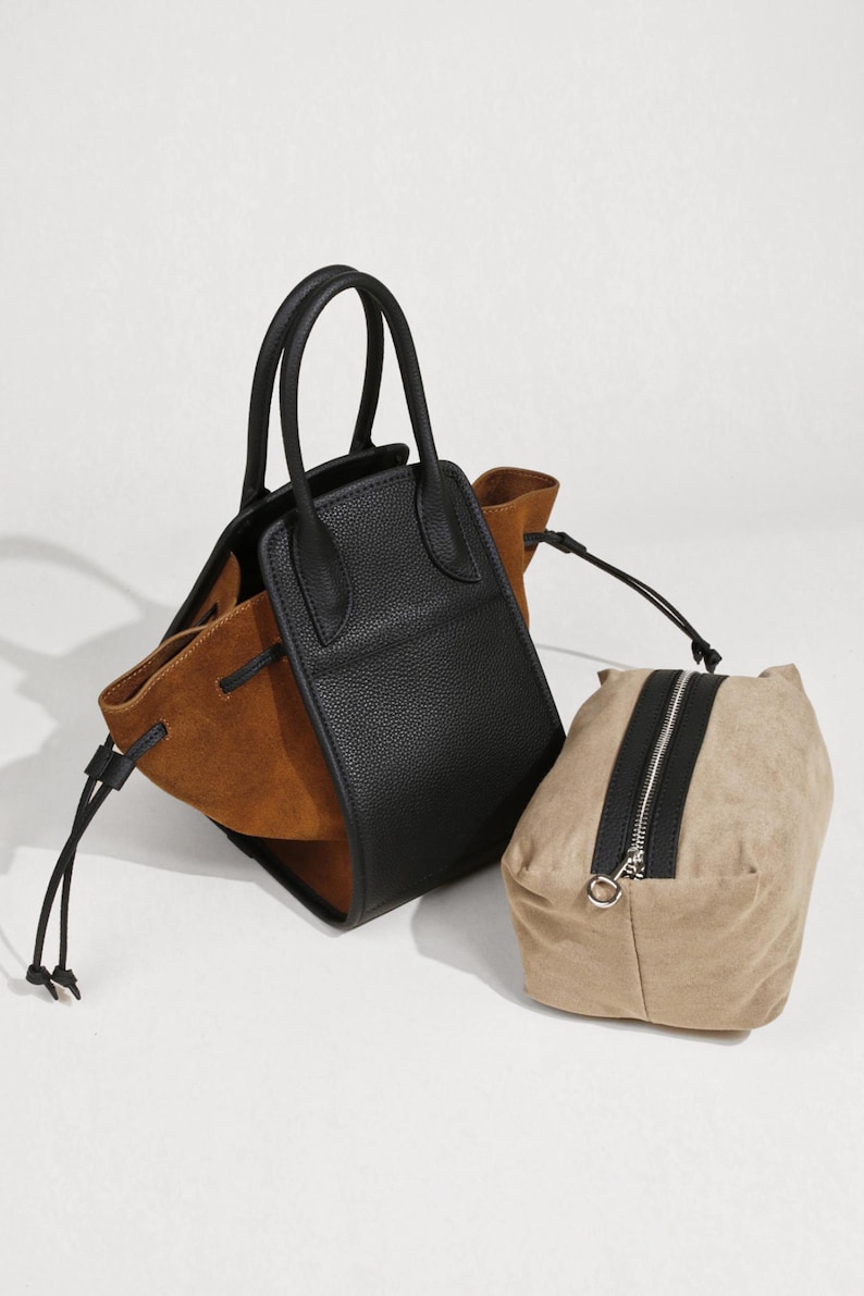 K&ouml;nnte beinhalten: Eine schwarze und braune Ledertasche mit Kordelzug und einer separaten braunen Tasche.