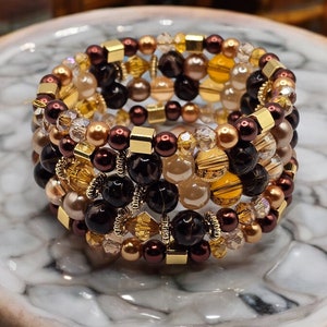 May include: Multi-layered bracelet with brown, gold, and clear beads. The bracelet is made of various materials, including glass, metal, and wood.