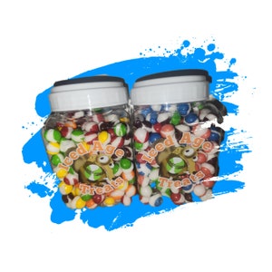 Può includere: Due barattoli di plastica trasparente pieni di caramelle colorate, ciascuno con un coperchio bianco e la scritta "Iced Age Treats". Le caramelle sono un mix di rosso, bianco, giallo, verde e blu. I barattoli sono su uno sfondo blu a spruzzi di vernice.