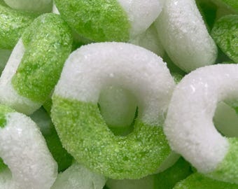May include: Close-up of a pile of ring-shaped candies. The candies are white with a green section, and covered in a sugary coating. The image is brightly lit, showing the texture of the candies.