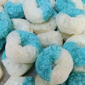May include: Close-up of a pile of blue and white frosted, ring-shaped candies. The candies are covered in a sugary coating, with one half of each candy in a bright blue color and the other half in white.