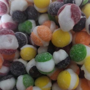 Può includere: Primo piano di una varietà di caramelle colorate a forma di palla. Le caramelle sono ricoperte di glassa bianca e hanno strisce e macchie di diversi colori. Le caramelle sono un mix di rosso, arancione, giallo, verde, blu e viola.