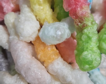 May include: A close-up of colorful, textured candies in various shapes. The candies are in shades of pink, yellow, green, orange, and blue. The candies have a bubbly, irregular surface.