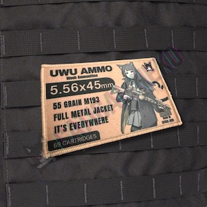 May include: A rectangular patch with the text "UWU AMMO" and "5.56x45mm". It features an anime-style illustration of a character holding a rifle. The patch also includes the text "55 GRAIN M193 FULL METAL JACKET IT'S EVERYWHERE" and "69 CARTRIDGES".