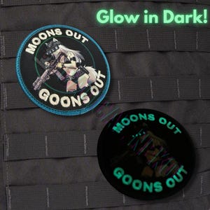 Può includere: Due toppe rotonde con la scritta "MOONS OUT GOONS OUT" e un personaggio in stile anime con un fucile. Una toppa ha un bordo blu, l'altra si illumina al buio. Il testo "Glow in Dark!" è sopra le toppe.