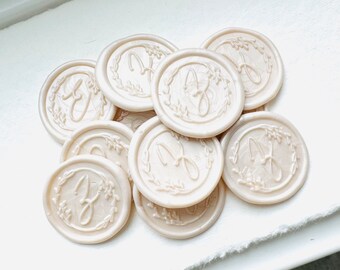 May include: A cluster of ivory wax seals, each displaying a cursive letter "J" within a floral wreath. The seals have a pearlescent finish, and are arranged in a slightly overlapping pattern. The overall effect is one of elegance and detail.