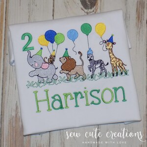 Puede incluir: Una camiseta blanca con un dise&ntilde;o bordado de un elefante gris, un le&oacute;n marr&oacute;n, una cebra blanca y negra y una jirafa, todos con gorros de fiesta. Los animales sostienen globos de colores. El n&uacute;mero 2 y el nombre Harrison est&aacute;n bordados debajo.