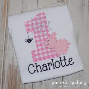 May include: White t-shirt with a pink gingham number 1, a pink pig, and a black spider hanging from a web. The name "Charlotte" is embroidered in black script. The words "sew cute creations" are at the bottom.
