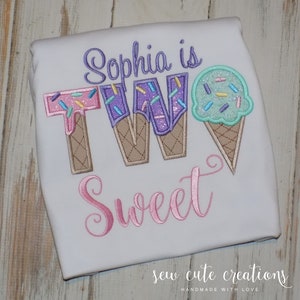 May include: A white t-shirt with the text "Sophia is TWO Sweet" embroidered in pink, purple, and green. The number two is made to look like ice cream cones with sprinkles.