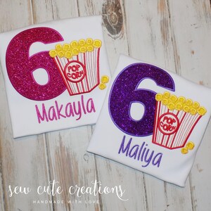 May include: Two white t-shirts with a pink and purple glitter number six and a red and white popcorn bucket. The shirts are personalized with the names Makayla and Maliya.