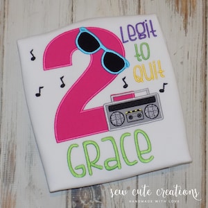 May include: A white t-shirt with a pink number 2, blue sunglasses, a gray boombox, and the text "Legit to quit" in rainbow colors. The name "Grace" is written in green below the boombox.