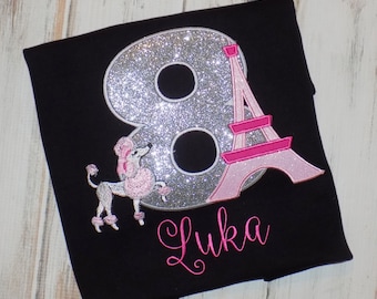 May include: A black t-shirt with a silver glitter number 8, a pink Eiffel Tower, and a pink poodle. The name "Luka" is embroidered in pink below the number. The shirt says "sew cute creations handmade with love".