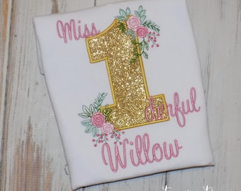 May include: White t-shirt with a gold glitter number one, decorated with pink and green floral embroidery. The shirt has the text "Miss Wonderful Willow" in pink script. The words "sew cute creations" are at the bottom.